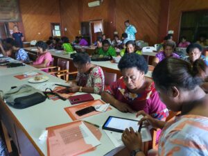 A group of women are in a building undertaking training on tablets to prepare them to take part in a mass drug administration.